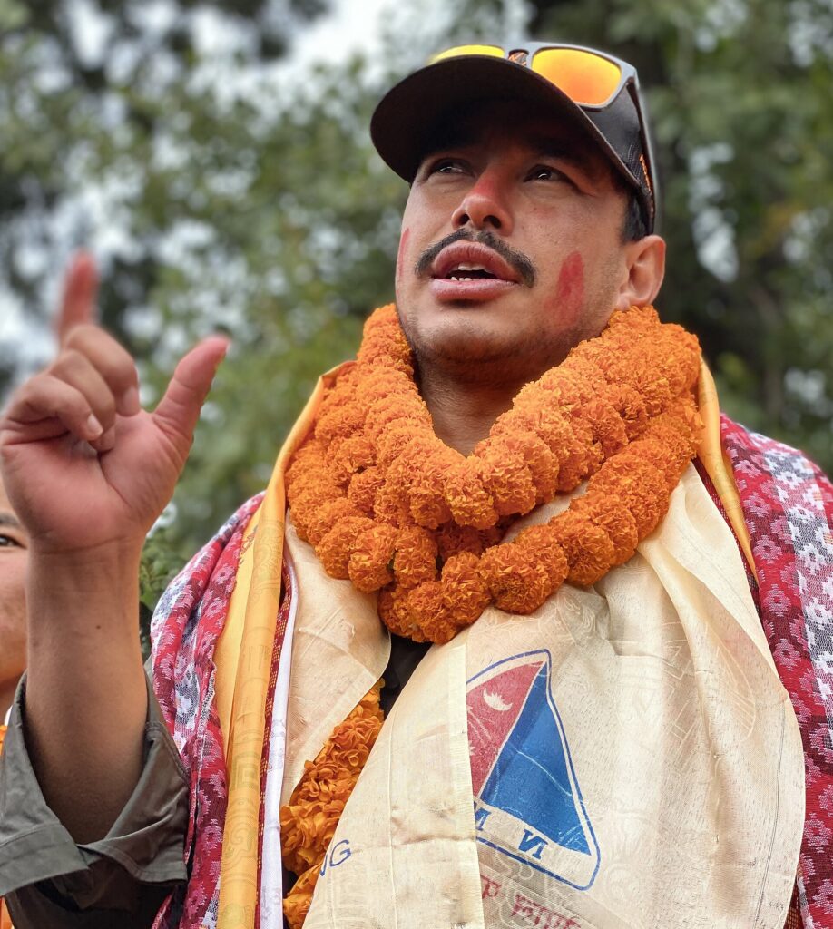 Nirmal Purja in a marigold garland and ceremonial scarves, speaking to a crowd in Kathmandu after his 2019 climbs.